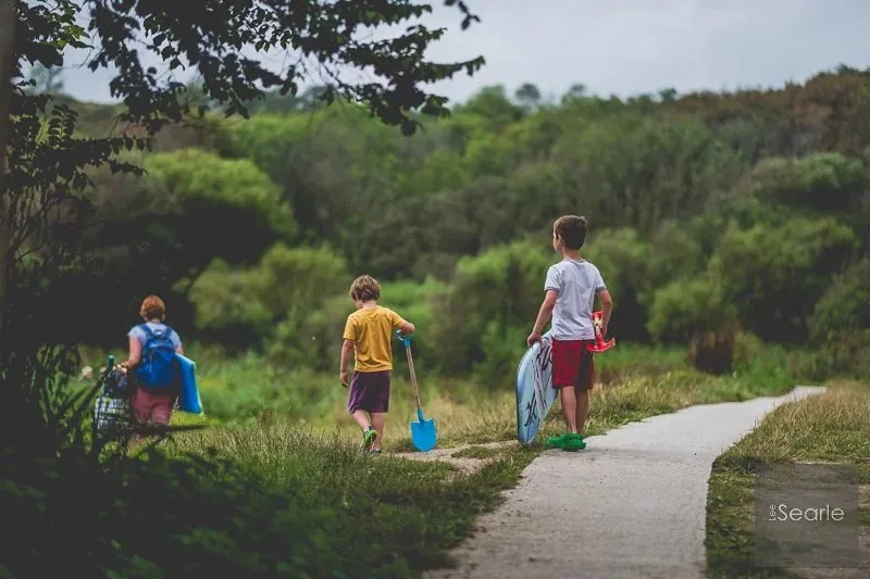 Children walking ahead with buckets and spades along a Cornish coast path on the way to the beach