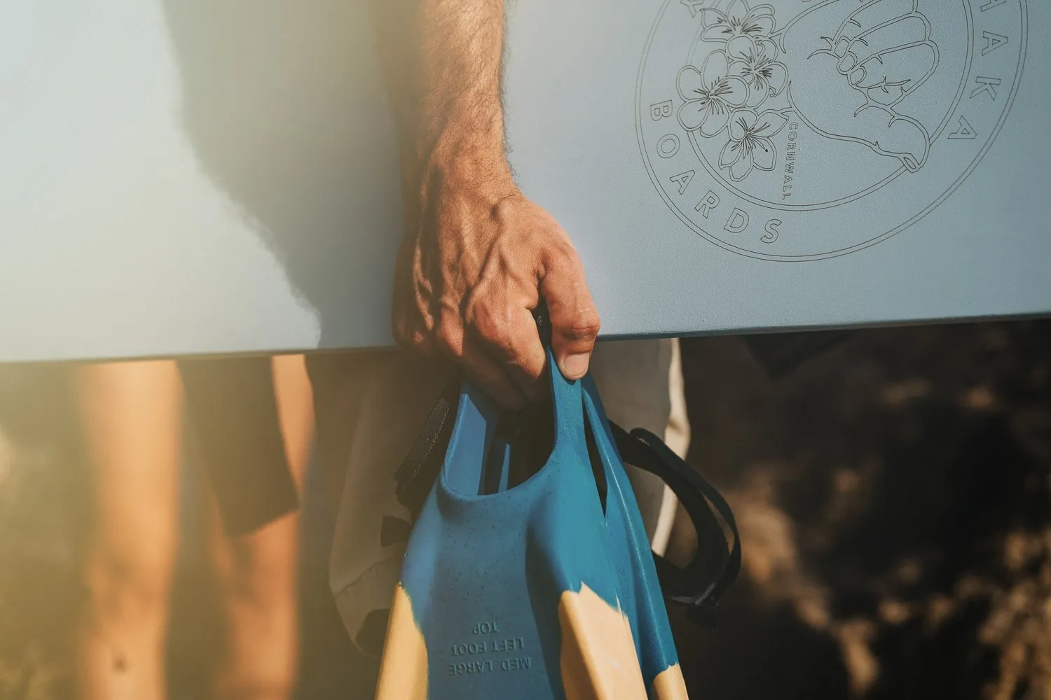 Close-up product detail of swim fins and a branded bodyboard on a Cornish beach