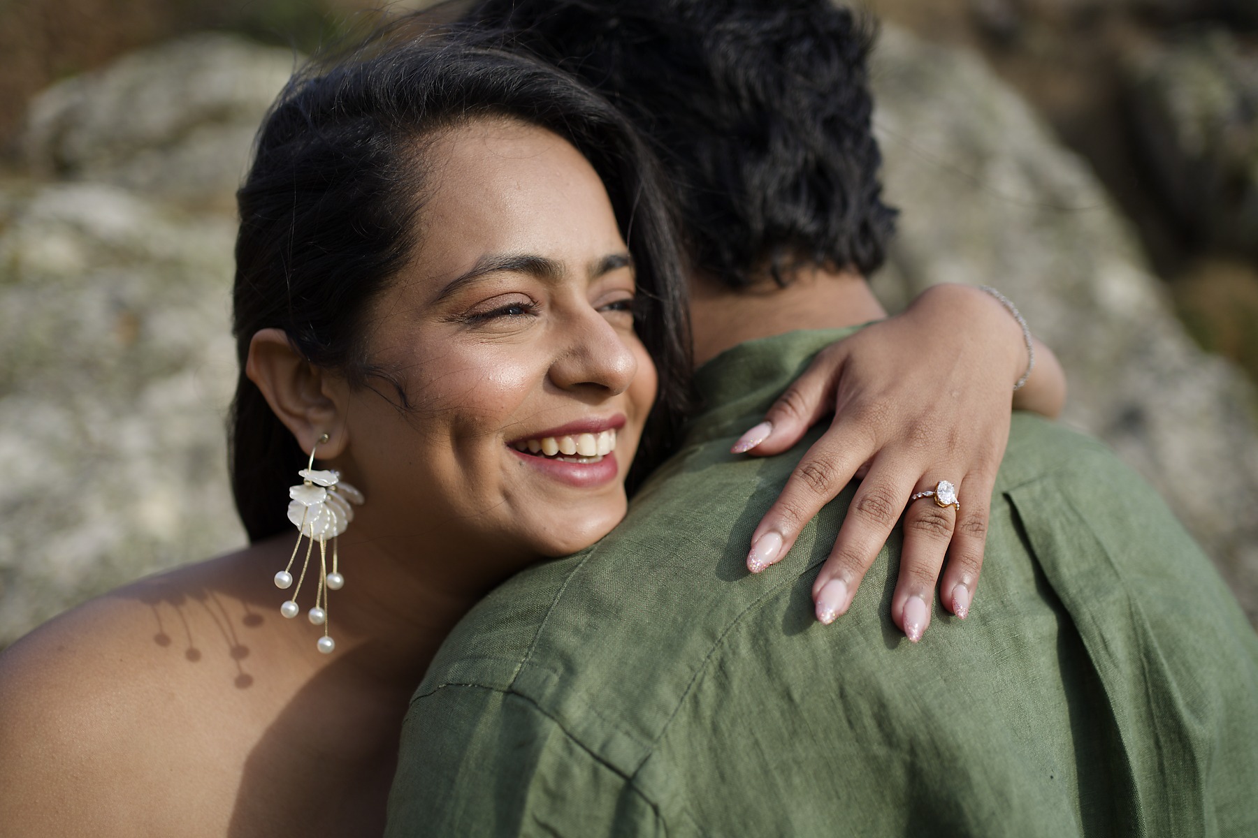 Engaged couple embracing beside coastal rocks after a proposal in Cornwall