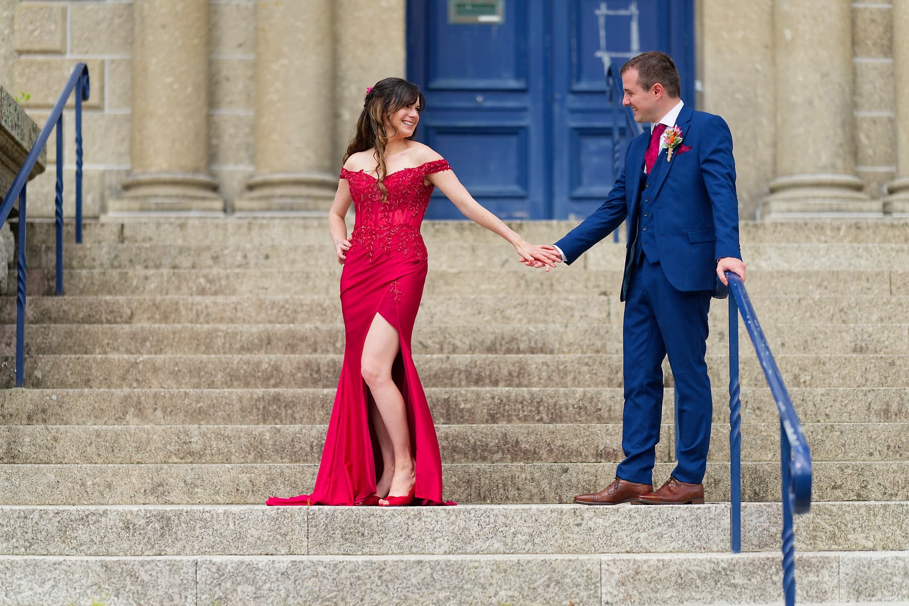 Bride in red and groom in blue on venue steps at a Cornwall wedding
