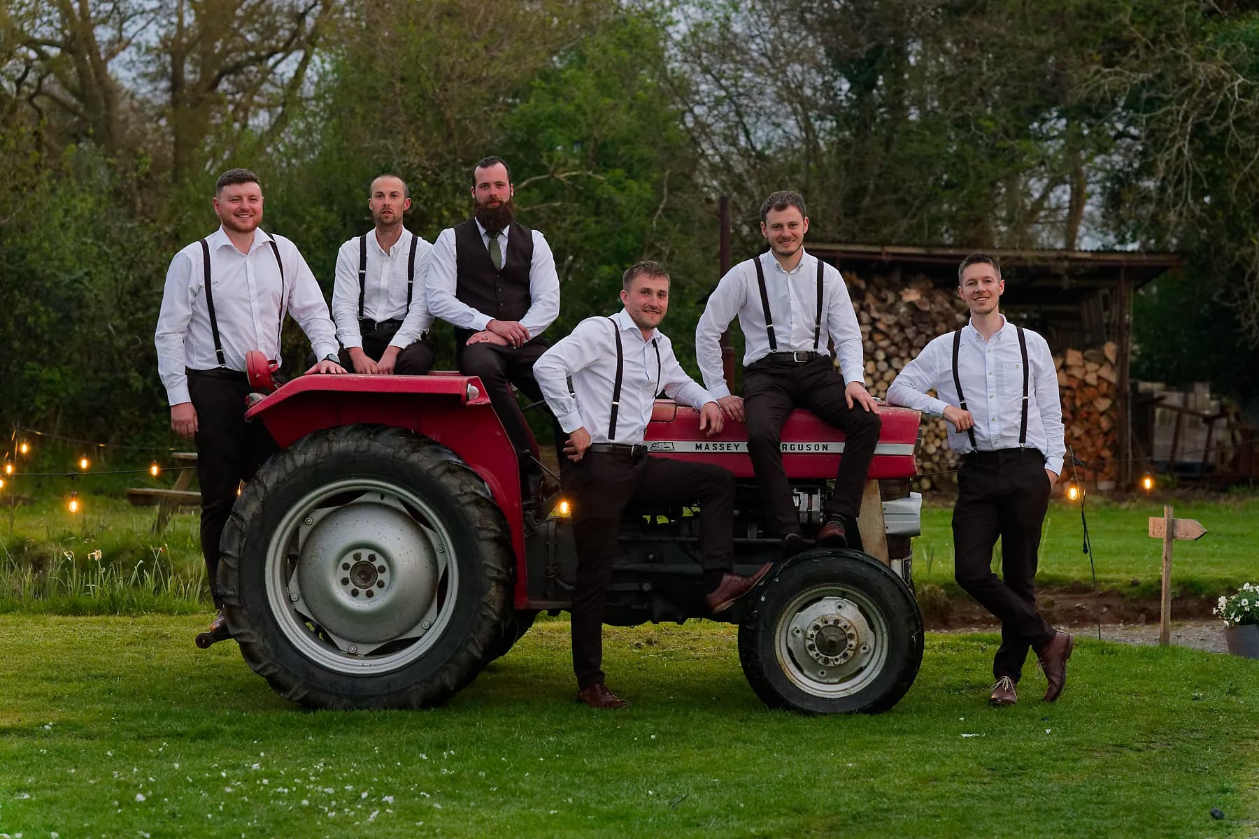 Groom and groomsmen gathered around a red tractor at a Cornwall farm wedding