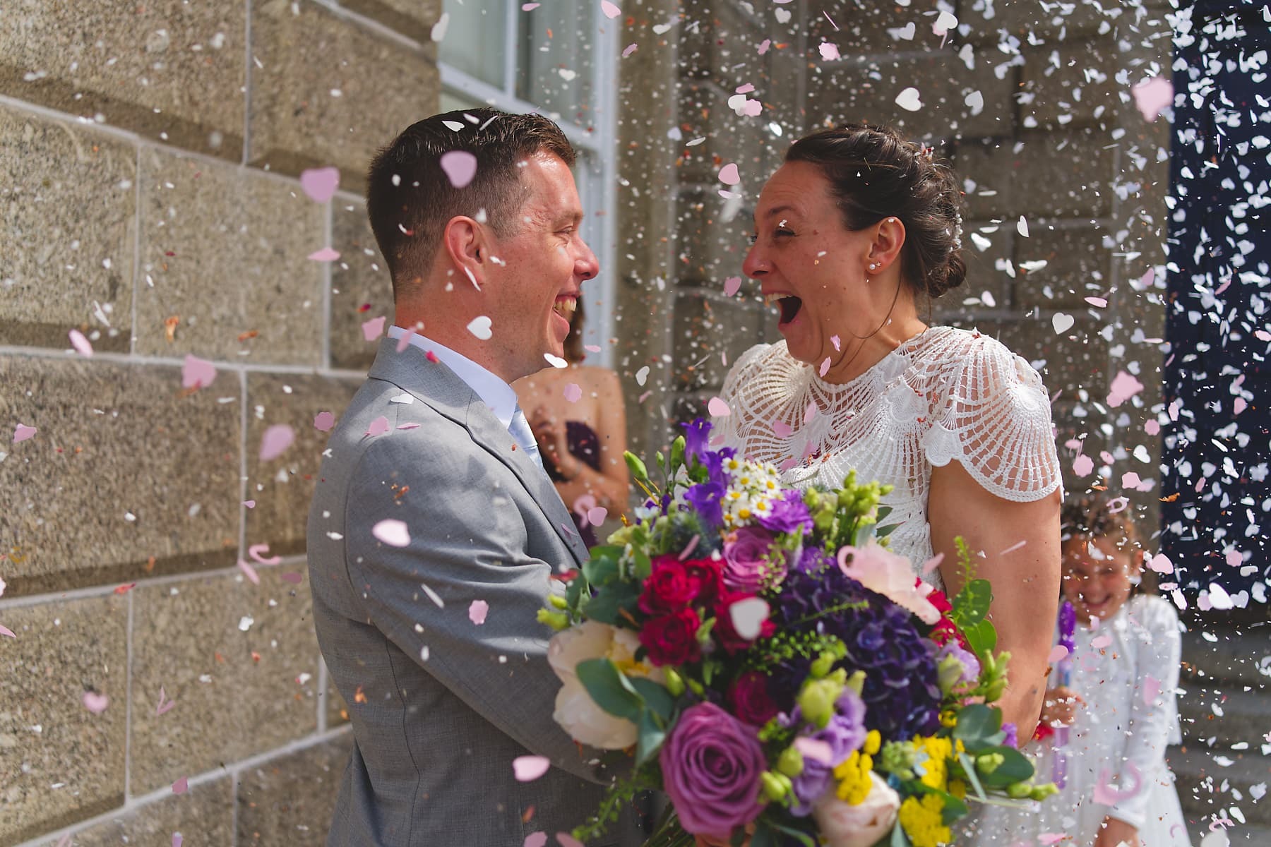 Newlyweds laughing beneath colourful confetti outside their Cornwall wedding