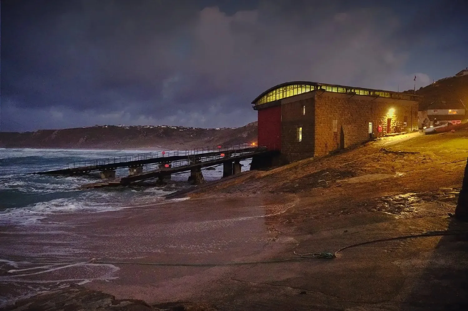Lifeboat station lit up at dusk above a stormy Cornish sea