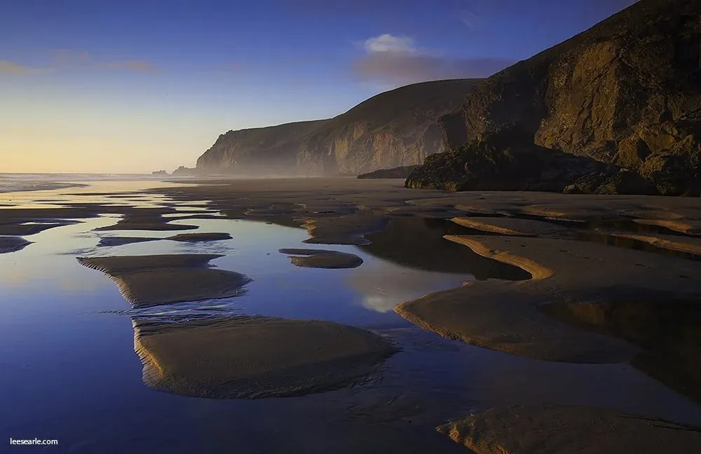 Rock pools reflecting first light beneath a headland on the north Cornwall coast