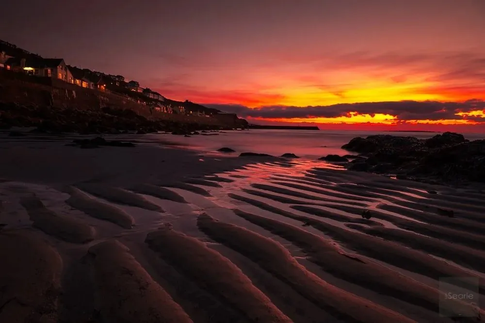 Rippled sand glowing under a blazing sunset over a Cornish fishing village